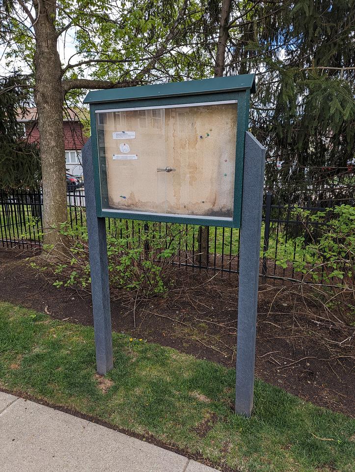 Freestanding Riverside Court notice board.  Green legs with a water damaged cork backing.