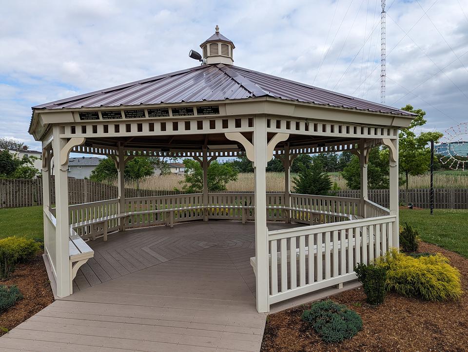 Off-white gazebo with brown metal roof.  The names of several servicemembers are visible above the gazebo entrance.