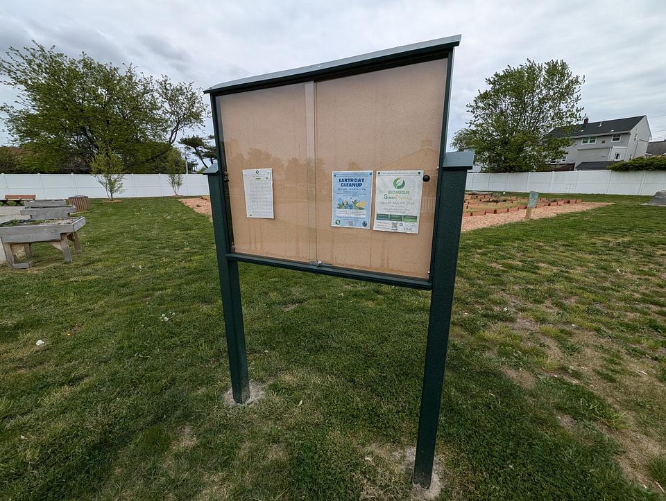 Freestanding notice board next to the community garden plots at Imagine Garden. Green legs with a cork backing.