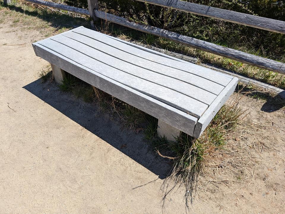 A grey composite bench with a wooden fence partially visible behind it