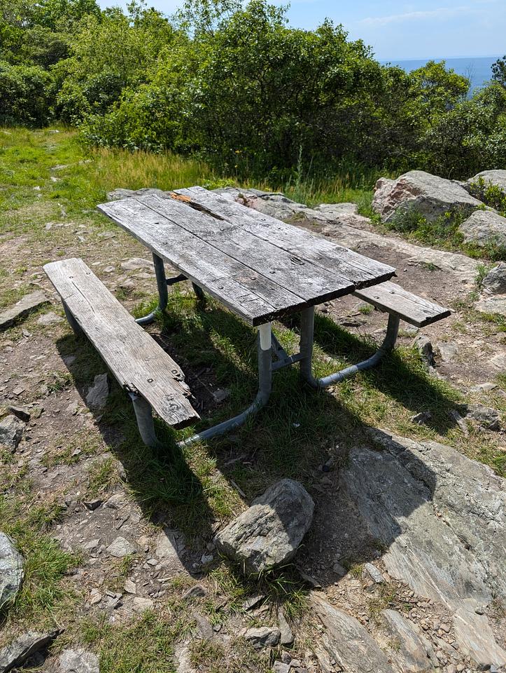 An old picnic table made of wood and metal.  The wood is falling apart and missing several pieces.